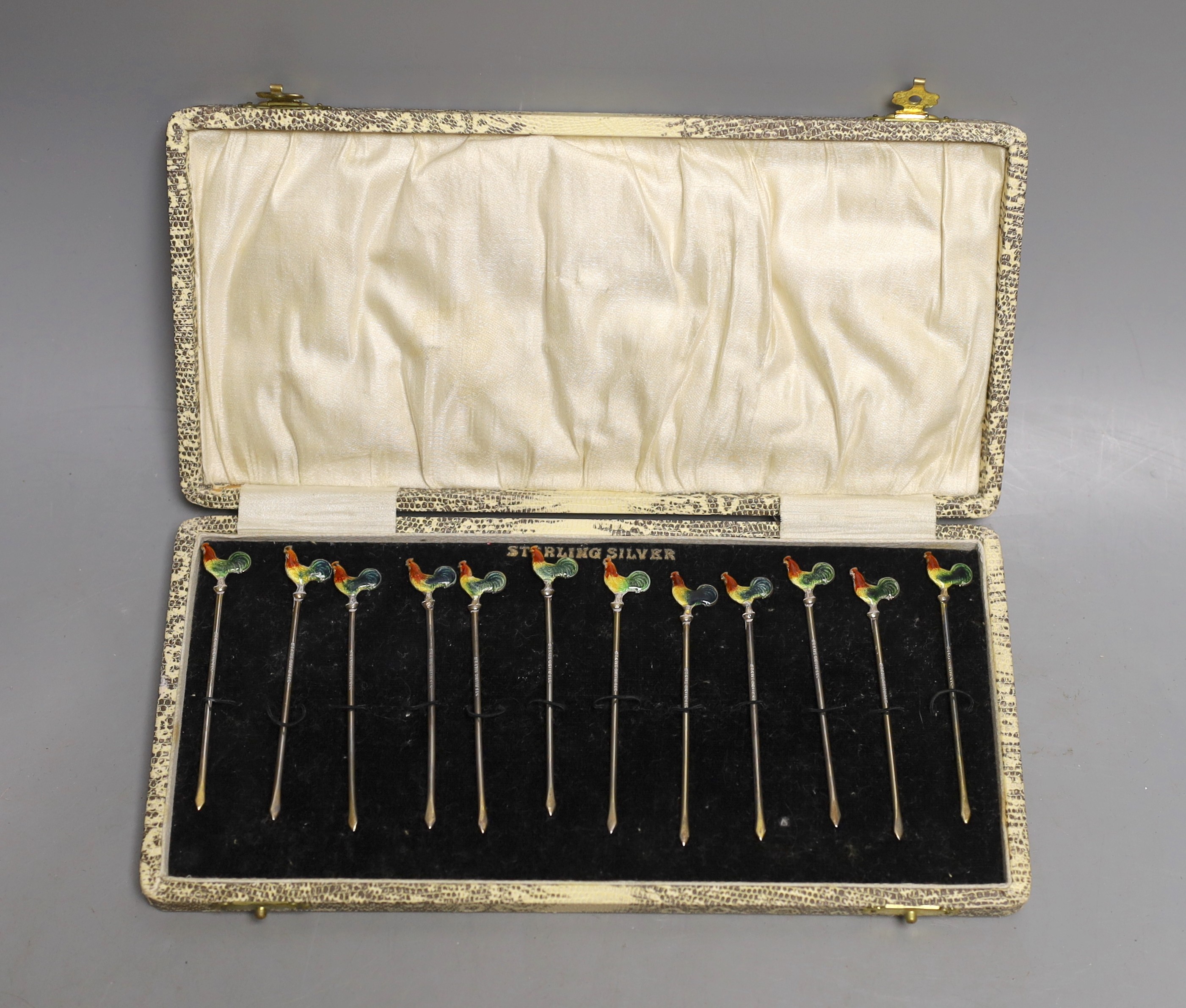 A cased set of twelve sterling and polychrome enamel cocktail sticks, the terminals modelled as cockerels, 80mm.